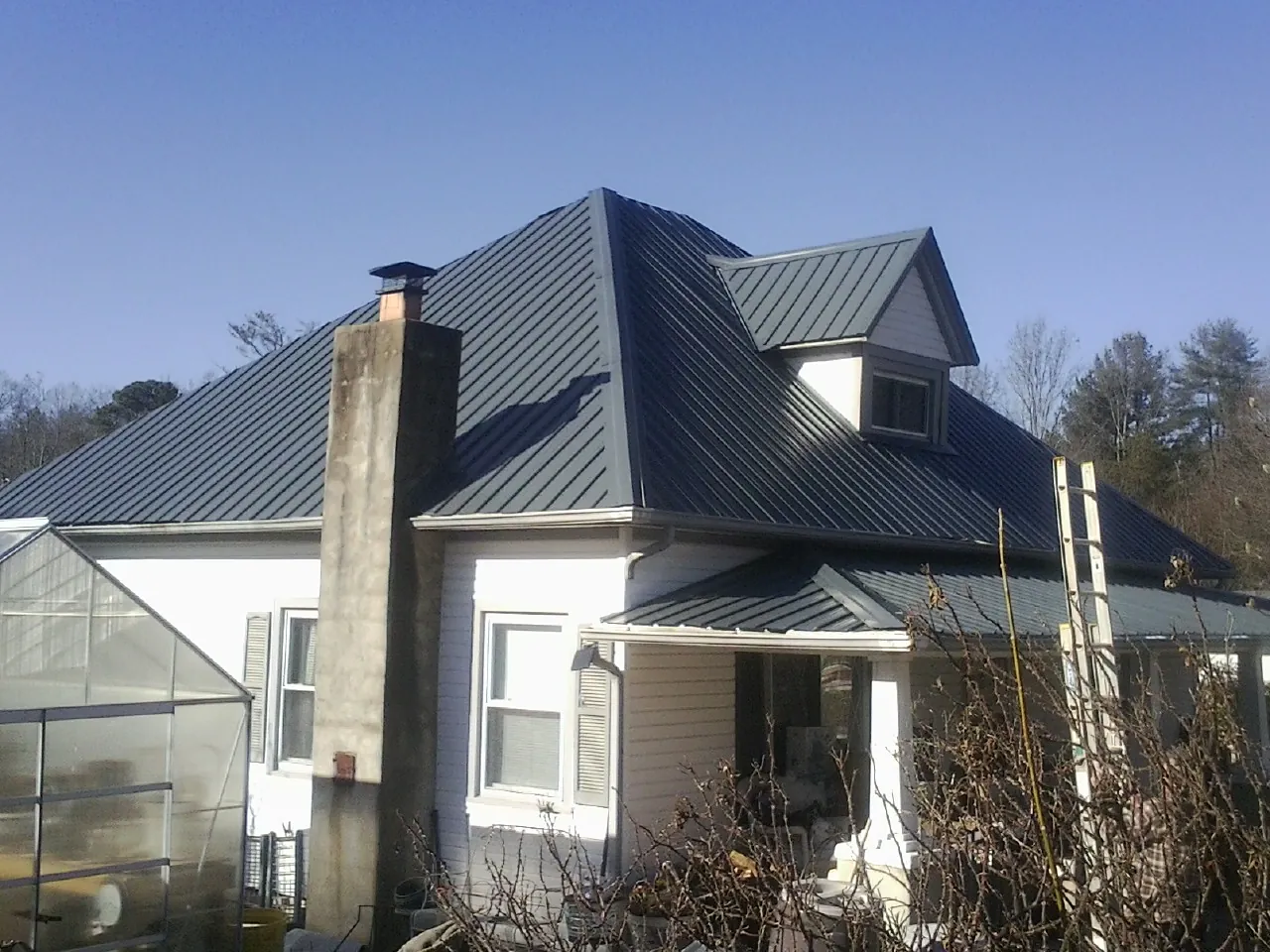 Dark blue standing seam metal roof on a white farmhouse with dormer — Slate & Tile Roof Repair by Roofing Brothers in Spring Glen