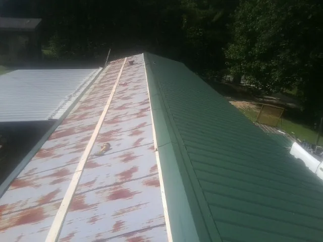 Old rusted panels beside newly installed green metal roofing — Wind Damage Roof Repair by Roofing Brothers in Spring Glen