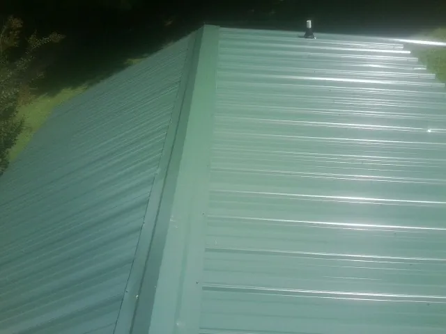 New green metal panels meeting at the ridge of a roof — Flat Roof Repair work by our crew in Spring Glen