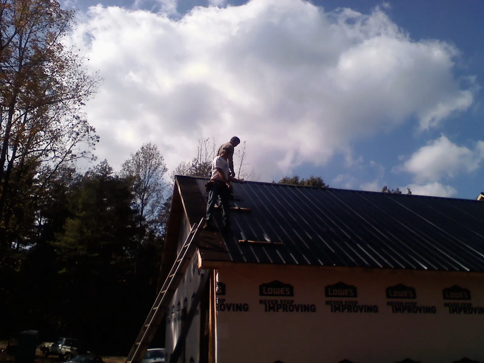 Roofer fastening dark metal panels high against a cloudy sky, from a Roof Inspection job in Spring Glen